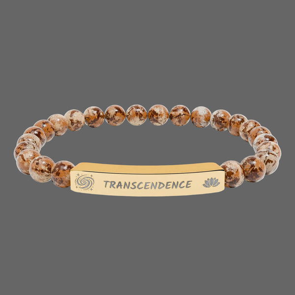 A beaded stretch bracelet featuring brown and beige marbled beads with a central gold-toned metal ID plate engraved with the word 'TRANSCENDENCE' and small spiritual symbols.