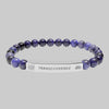 Beaded bracelet with a silver tag saying Transcendence with galaxy and lotus symbols