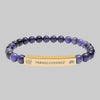 Beaded bracelet with a gold tone tag saying Transcendence with galaxy spiral and lotus symbols