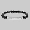 Black beaded bracelet with a silver tag saying Transcendence with galaxy and Lotus symbols