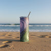 A tall, skinny insulated tumbler with a clear lid and straw, featuring an abstract swirling galaxy and yin yang art print in purple and green tones, .
