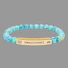 Turquoise beaded bracelet with a gold tone tag saying Transcendence with galaxy spiral and lotus symbols