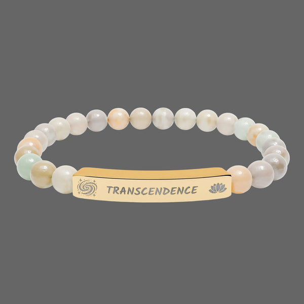 A beaded stretch bracelet featuring a central gold-toned bar engraved with the  spiritual word 'TRANSCENDENCE' and small lotus and spiral motifs. The beads are a mix of soft pastel tones including cream, peach, pale green, and light gray.