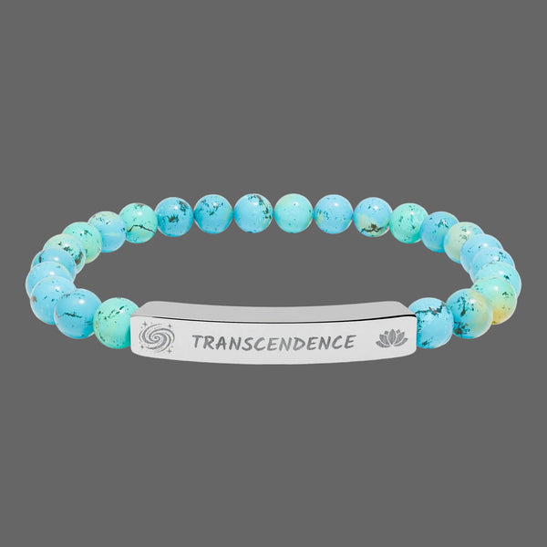 A beaded stretch bracelet featuring light blue and turquoise marbled beads with black veining, connected by a polished silver metal ID plate engraved with the word 'TRANSCENDENCE' and spiritual symbols of galaxy and lotus flower.